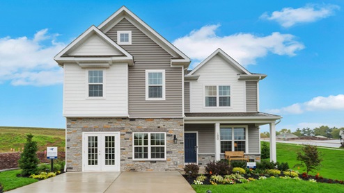 Two-story home with a covered front porch, horizontal plank siding in complimentary colors of taupe and cream with a stone water-table accent, and a sales center front on the two-car garage.