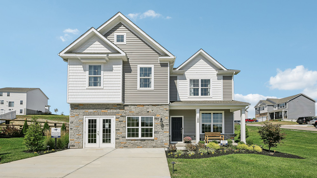 Two-story home with a covered front porch, horizontal plank siding in complimentary colors of taupe and cream with a stone water-table accent, and a sales center front on the two-car garage.