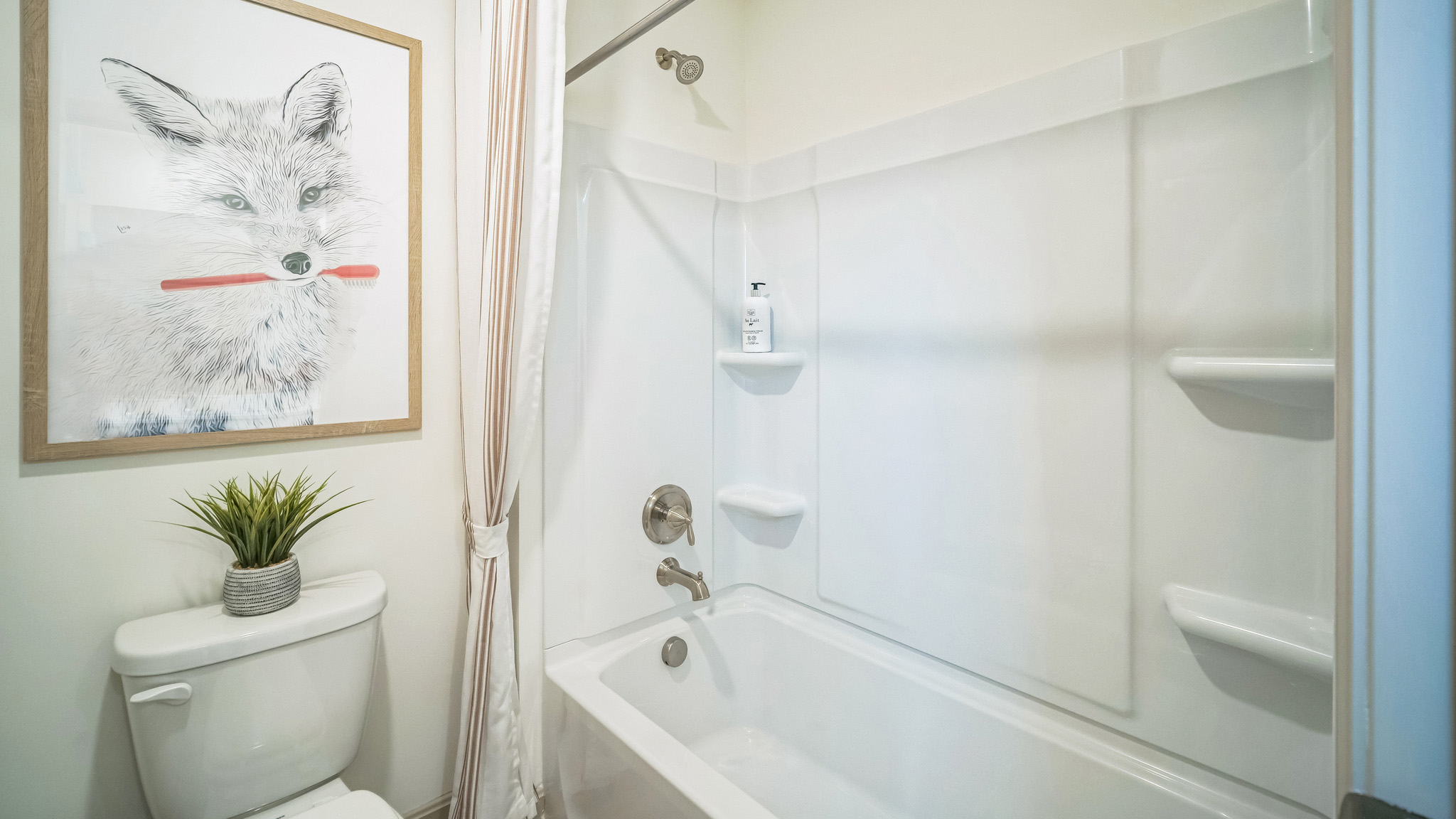 Secondary bathroom with a tub-shower insert and large artwork of a fox holding a toothbrush.