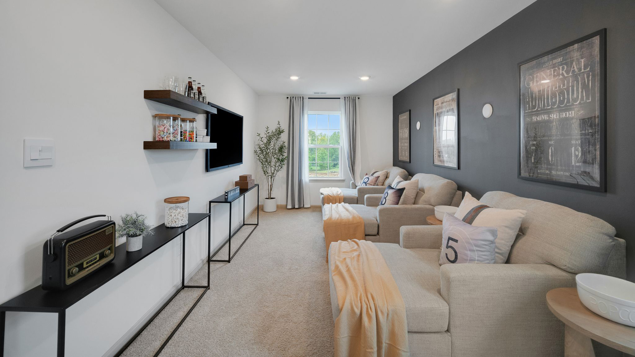 Entertainment room with three large, comfy chairs facing a wall-mounted TV with shelves full of candy, drinks, and popcorn.