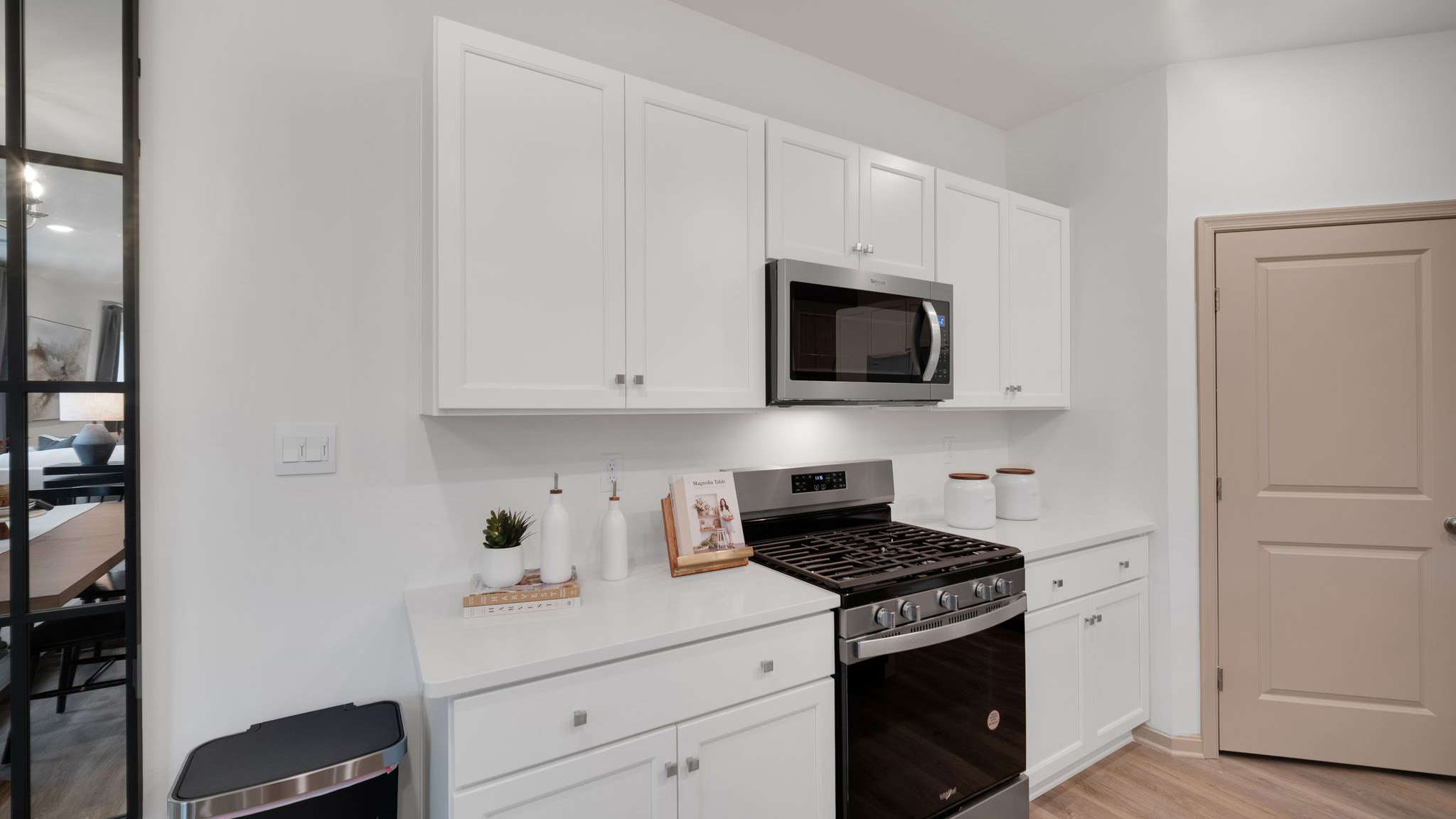 A stainless-steel gas range with venting microwave above set in a bank of white, shaker-style cabinets with white quartz countertops.