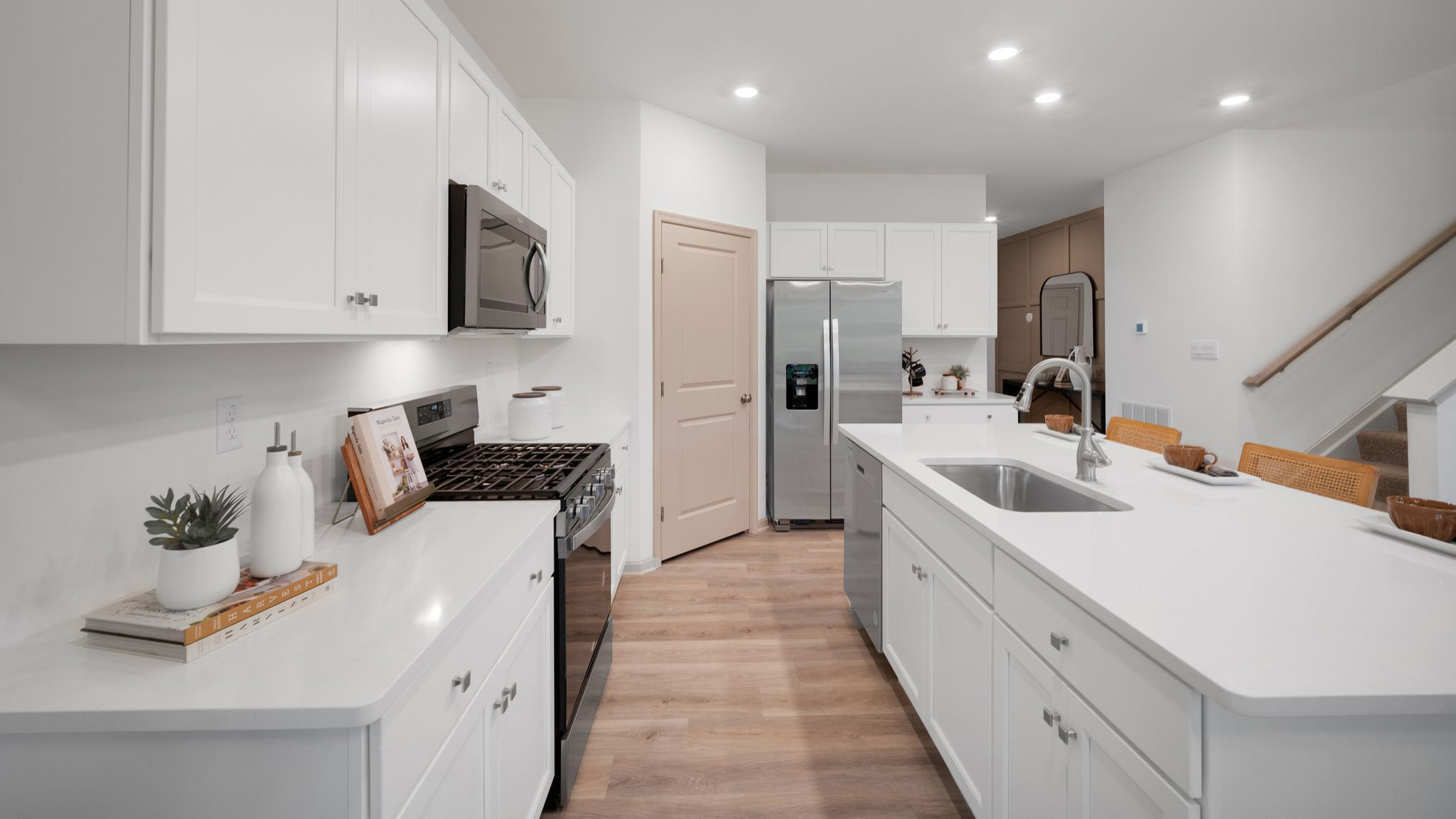 A spacious kitchen with white, shaker-style cabinets, quartz countertops, a large center island with undermount sink and seating for three, and a stainless-steel appliance package.