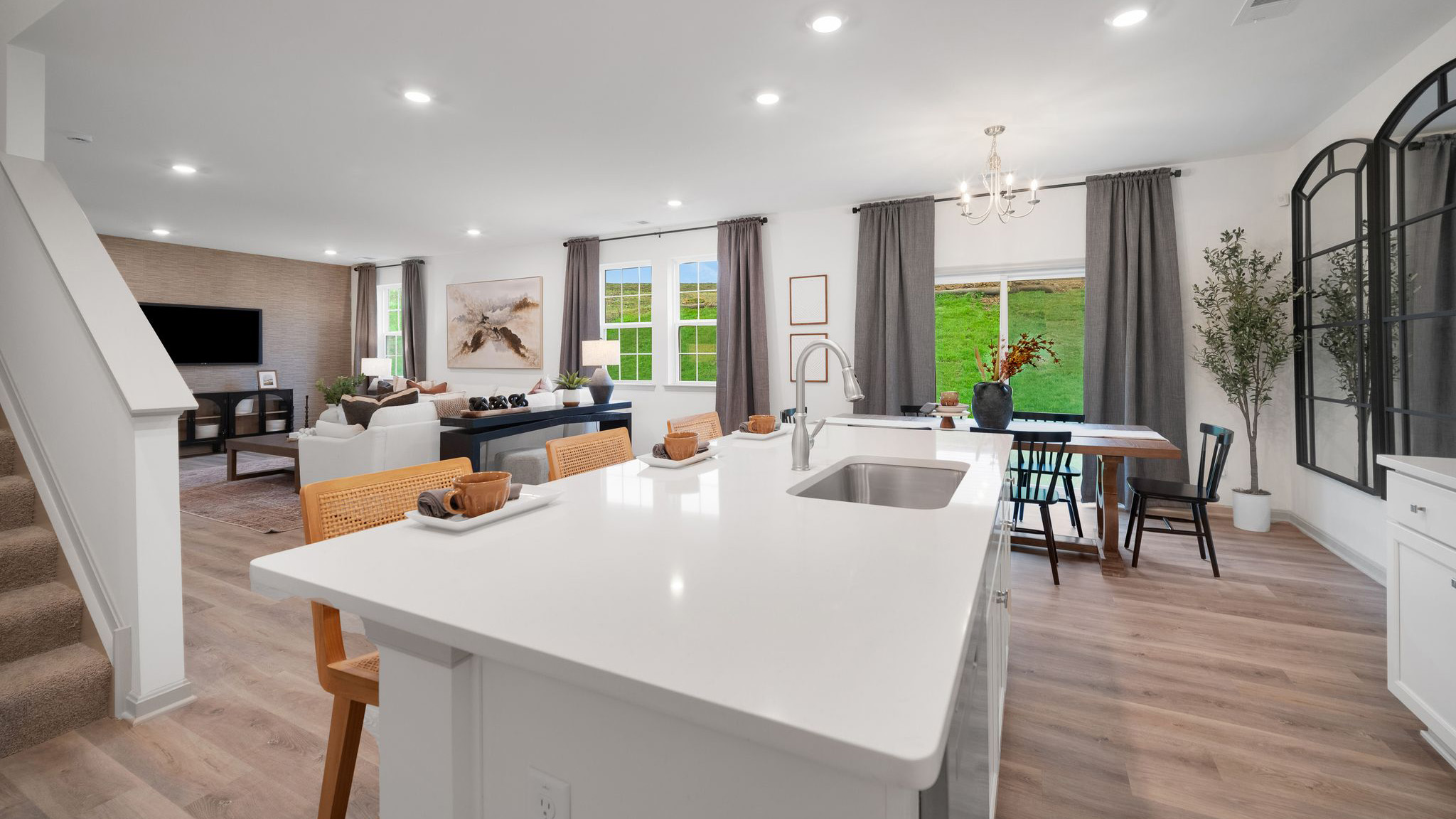 A spacious kitchen with white, shaker-style cabinets, quartz countertops, a large center island with undermount sink and seating for three, and a stainless-steel appliance package overlooking the adjoining dining space and living room.
