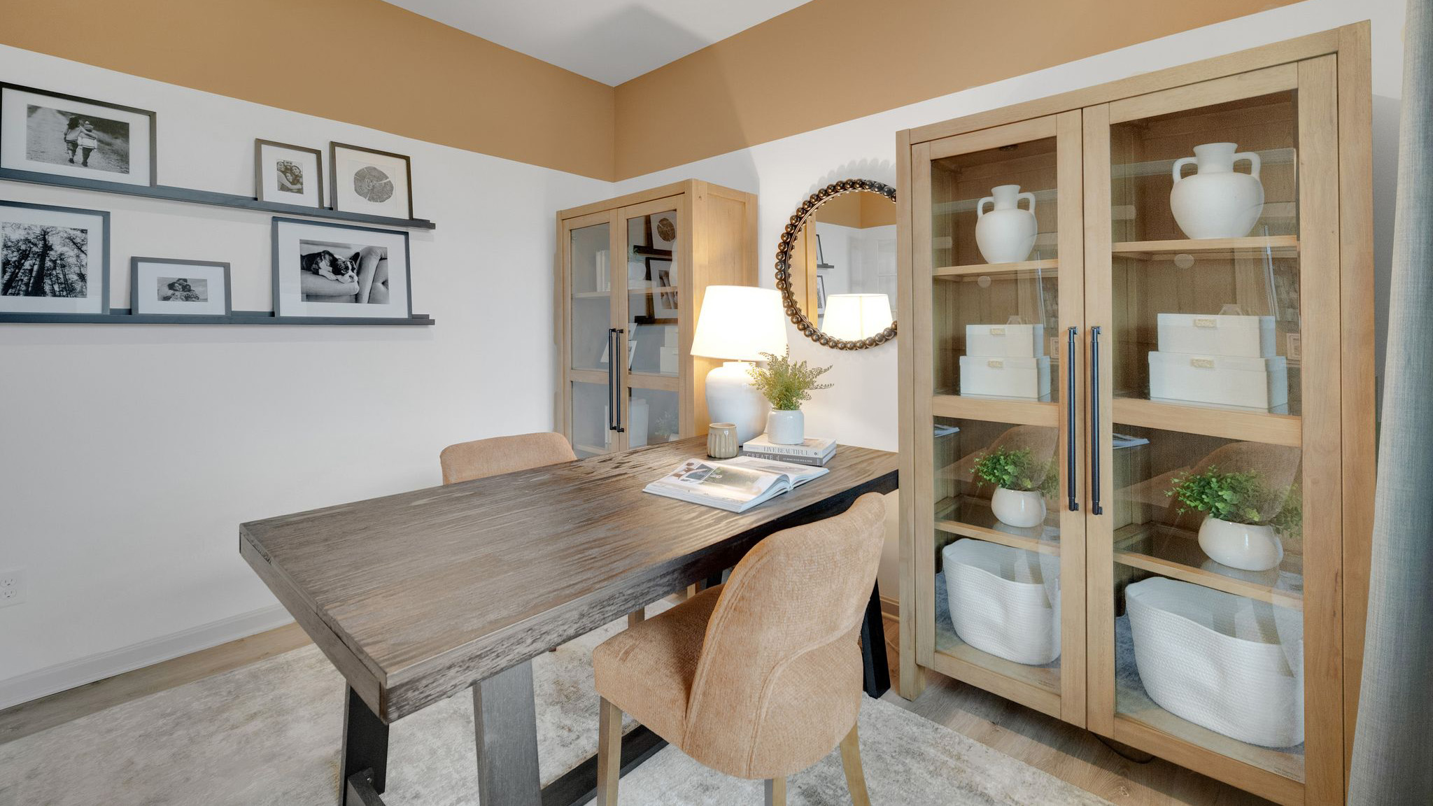 Secondary bedroom set up as an office with a desk with chairs on each side, two glass-fronted bookshelves, and picture rails displaying family photos on the back wall.