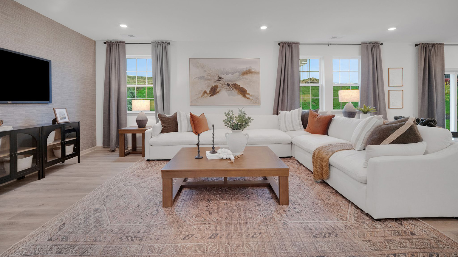 Living room with a large sectional sofa and coffee table arranged facing a wall-mounted tv above a storage console, all in front of a wall boasting three windows overlooking the back yard.