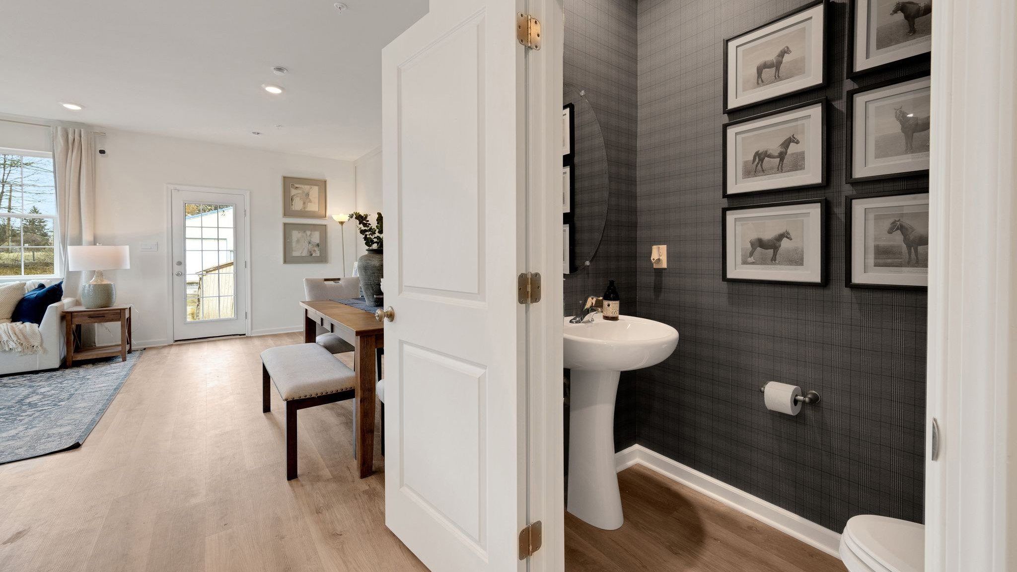 First floor hallway from the foyer with view of the half bath and part of the living area and dining area.