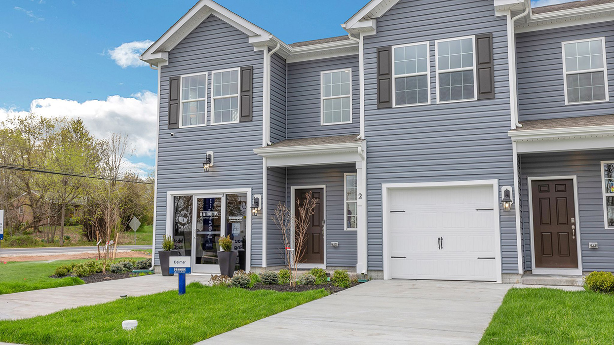 Exterior front image of the model townhome with dark gray horizontal paneling, black shutters, and a white single car garage.