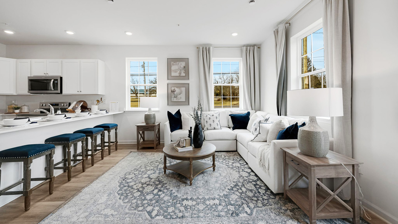 First floor living area with three large windows. To the left is the kitchen counter area with seating.
