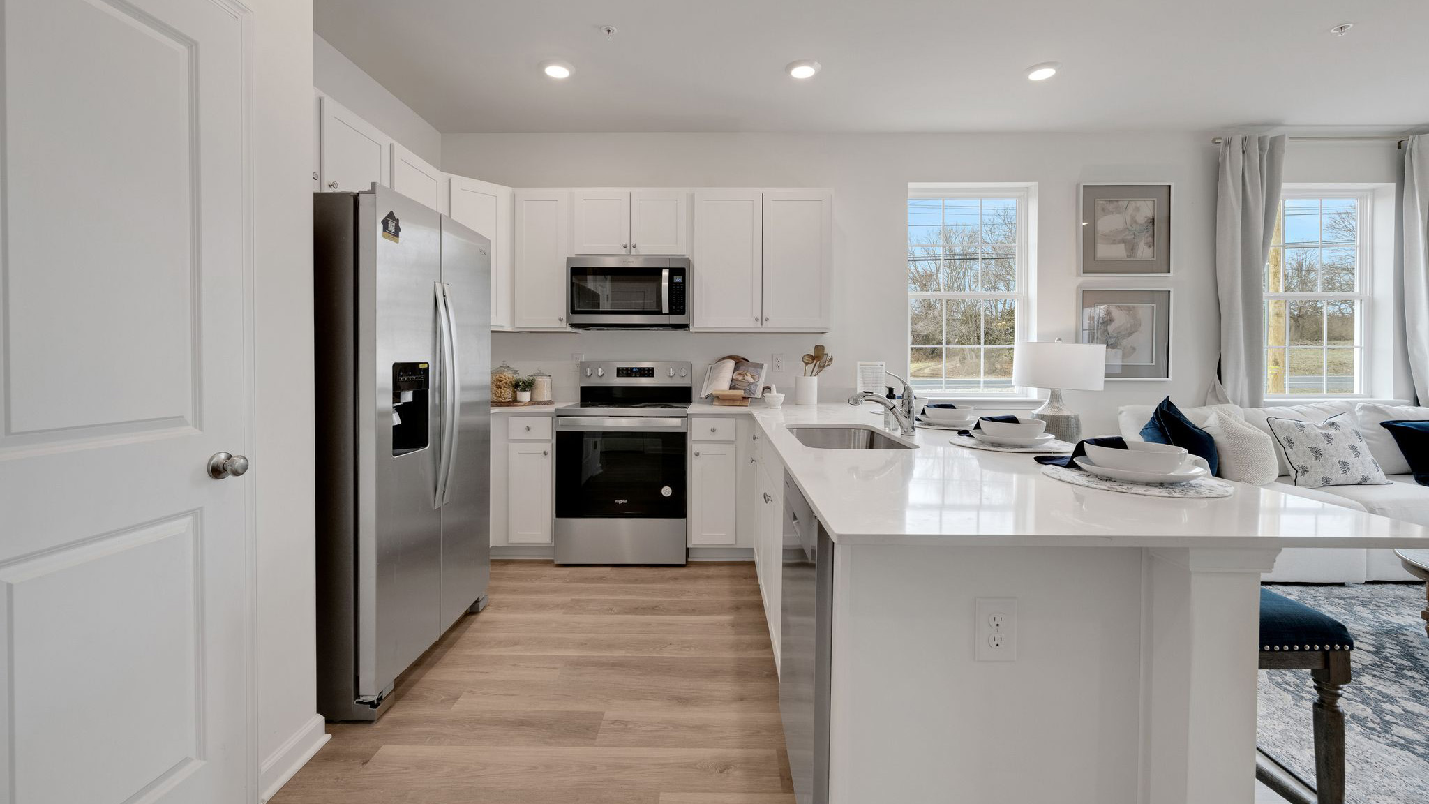 U shaped kitchen with stainless steel appliances and white counter tops and cabinetry.