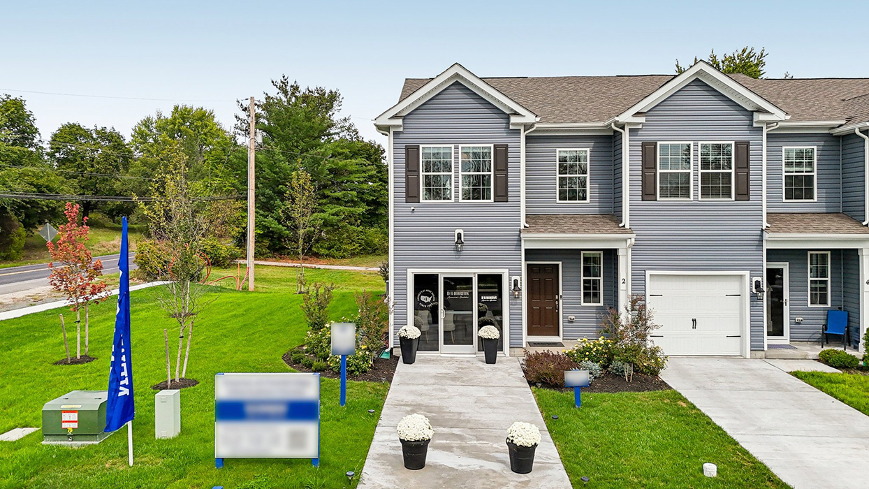 Exterior front image of the model townhome with dark gray horizontal paneling, black shutters, and a white single car garage.