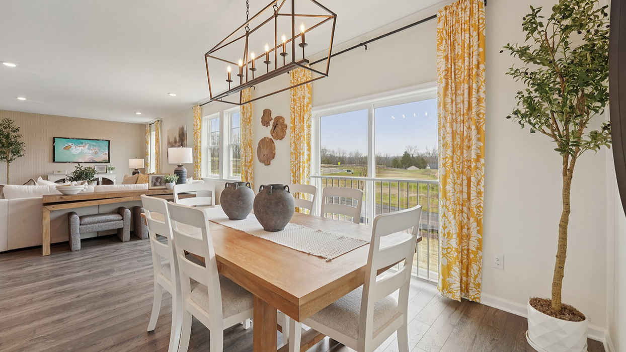 Dining space with a wooden table with a view towards the open-concept living pace and stairwell to the second floor.