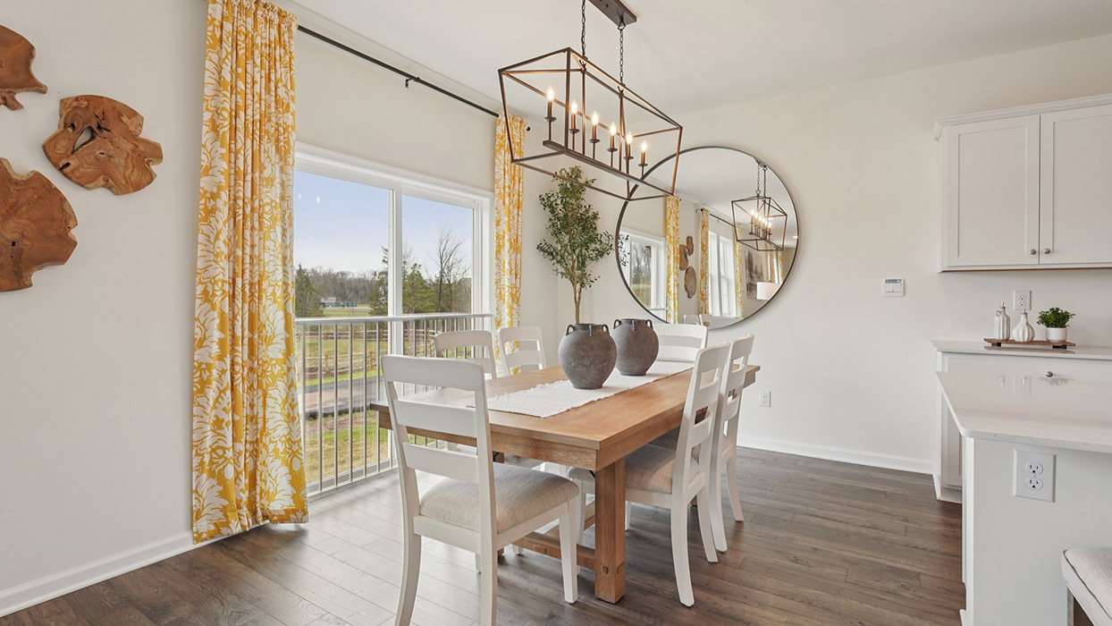 Dining space with a wooden table with a view towards the open-concept living pace and stairwell to the second floor.