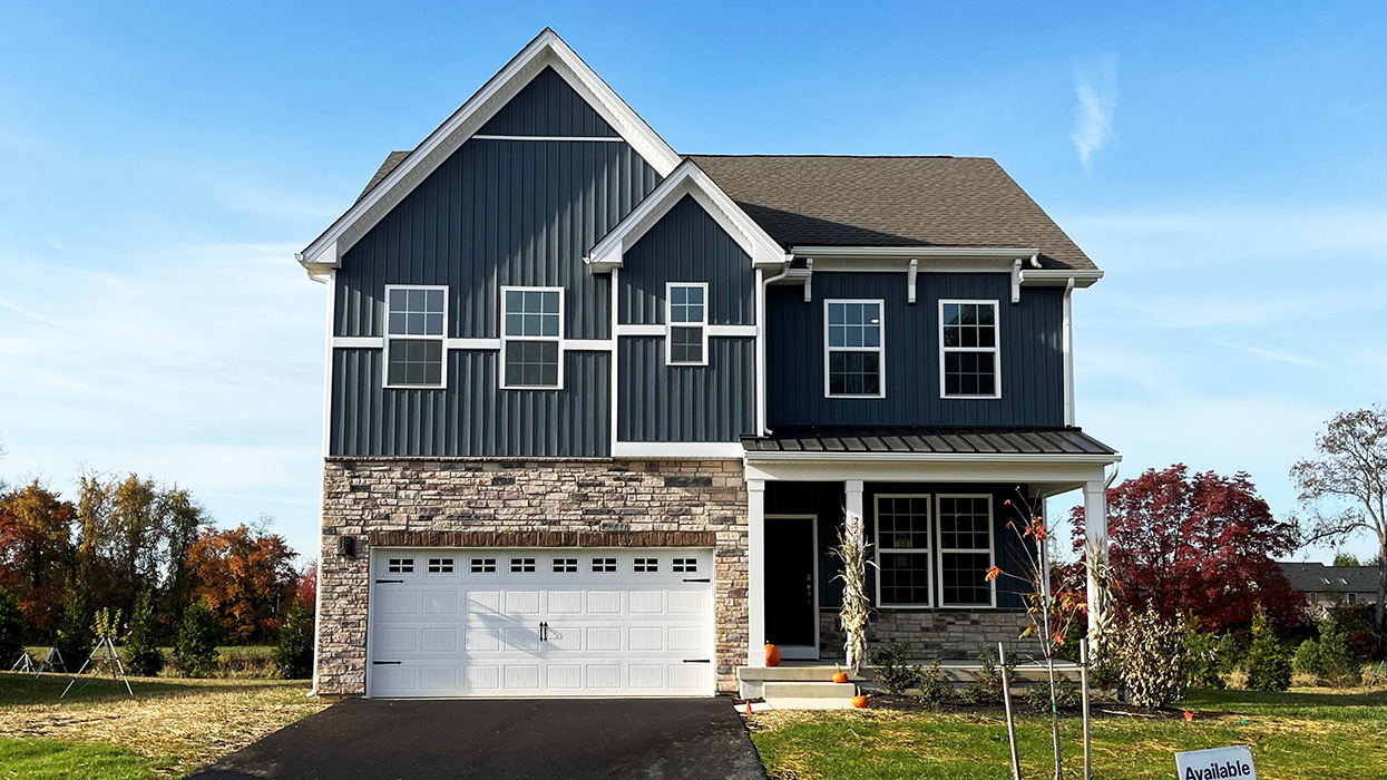 A photo of a two-story Penny home with navy board and batten siding, stone kneewall, and stone siding surrounding a white two car garage.