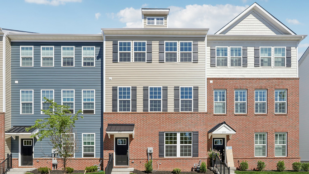 Exterior front image of a three story townhome with two car white garage in the back.