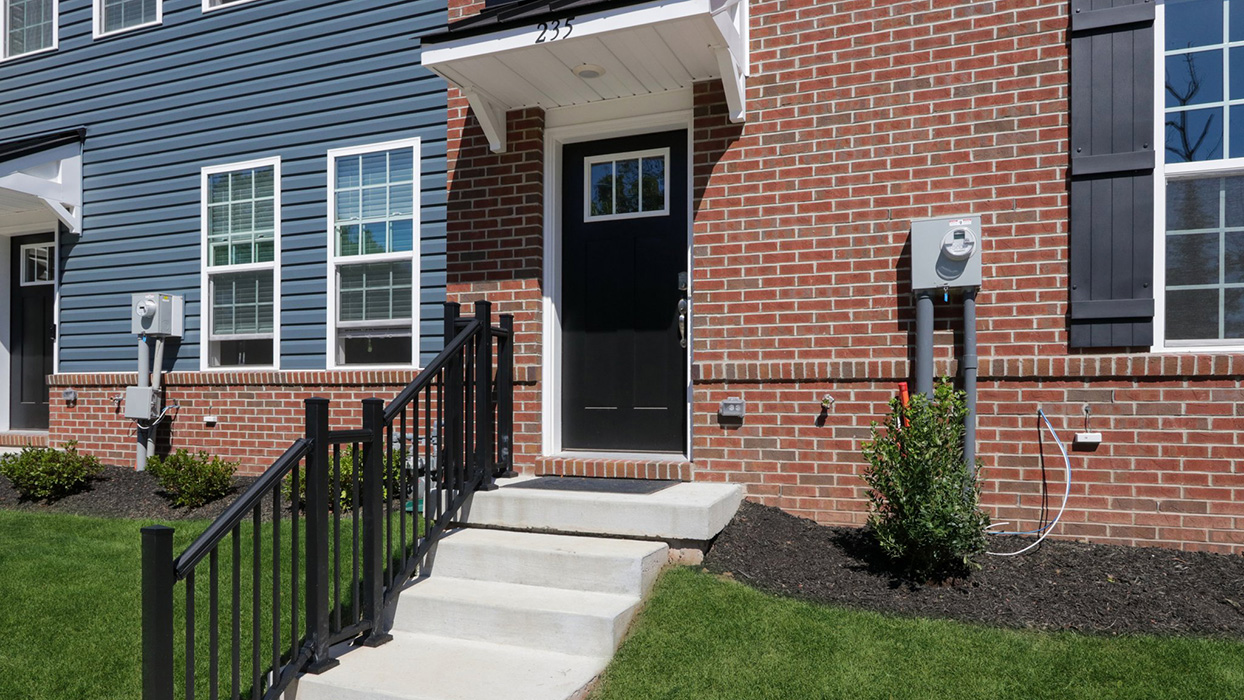 Exterior front image of a three story townhome with a black front door and several steps leading up to the front door.