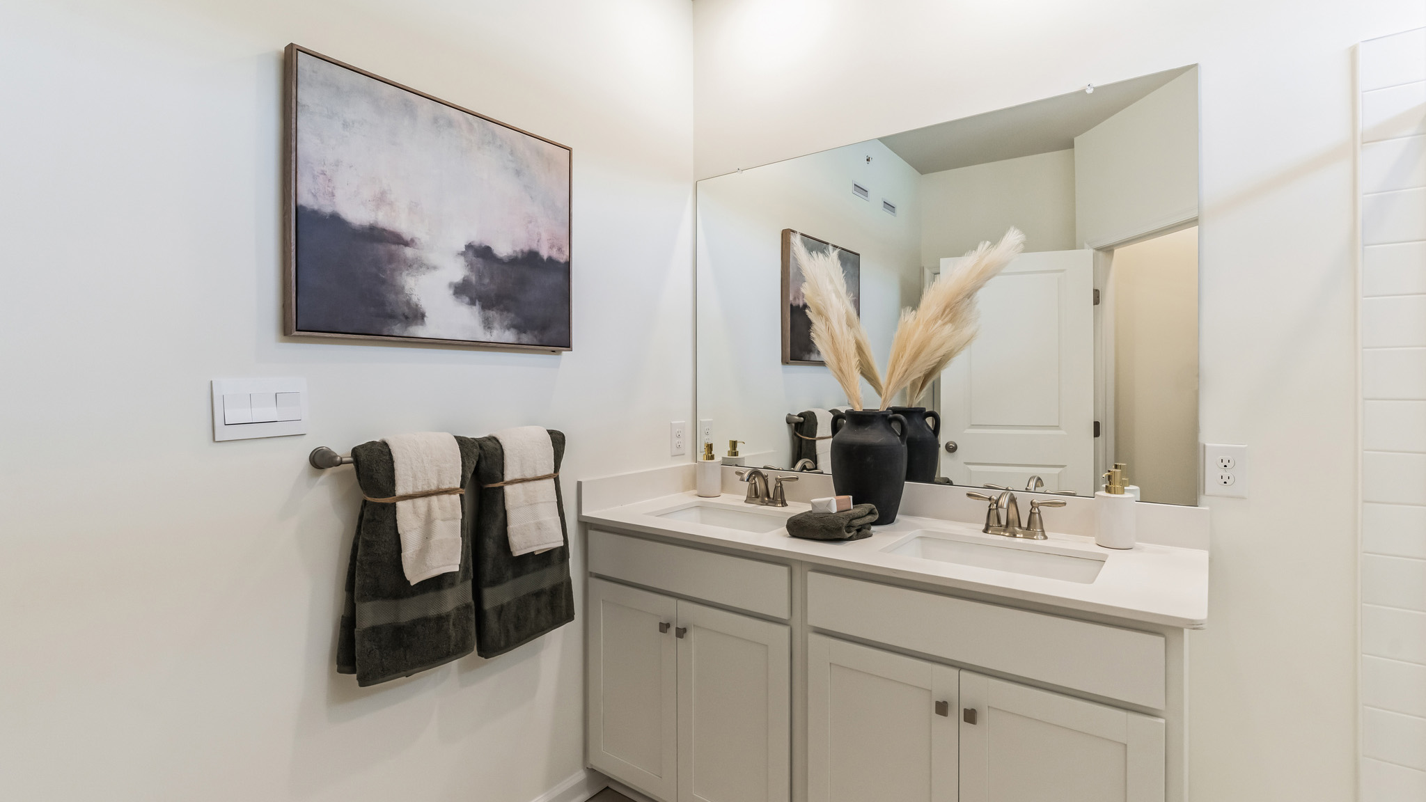 Different view of the connecting bath to the primary bedroom with double sink white vanity and glass door shower. A separate closet door to the toilet.