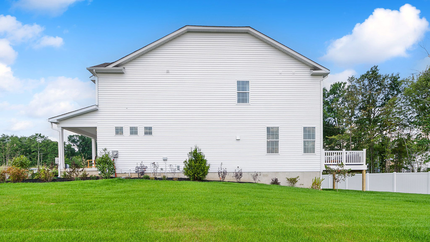 Exterior side image of the three story white horizontal paneling house with front porch and raised back porch.