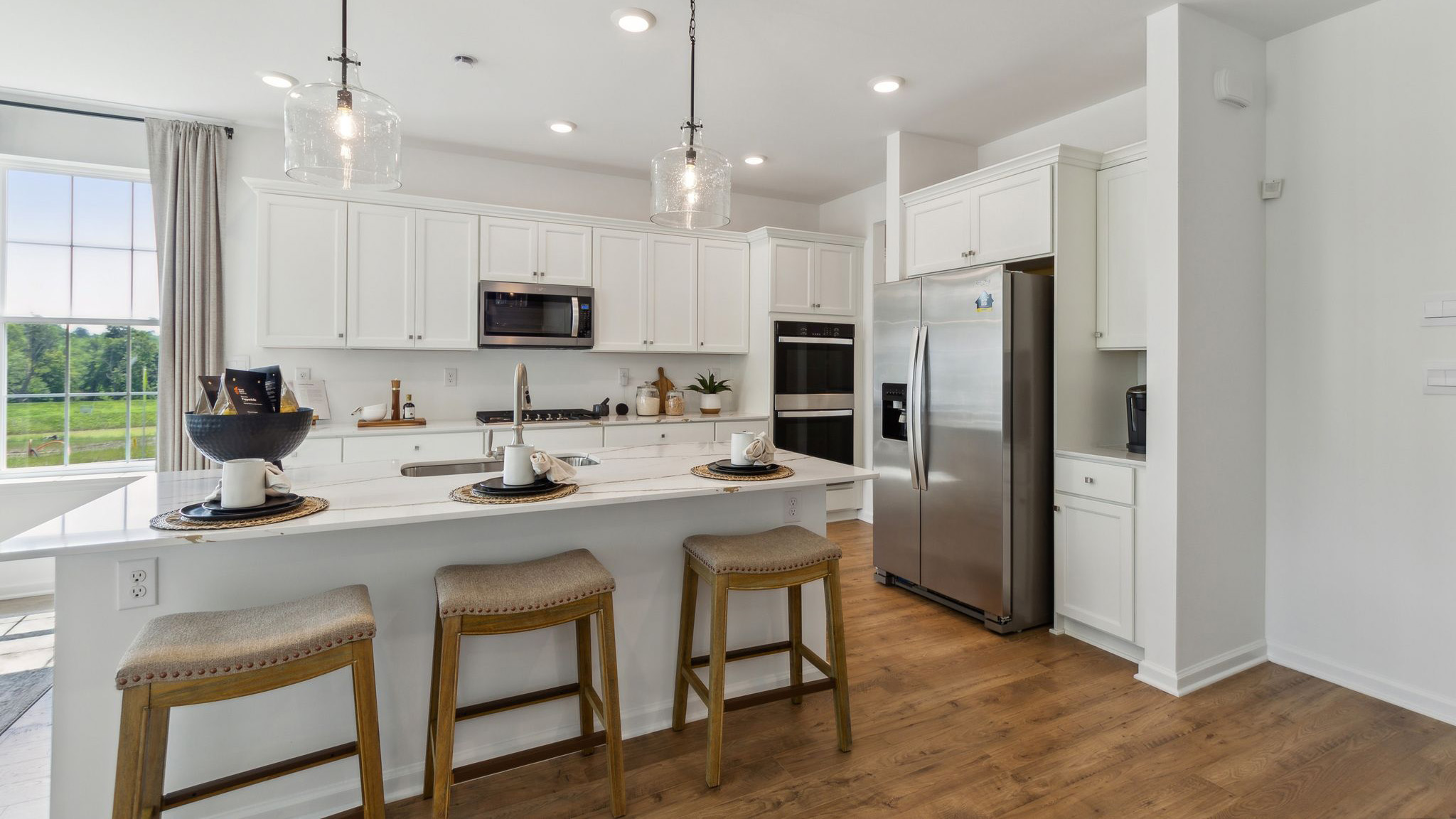 Spacious kitchen with large island, white counter tops, and white cabinetry and stainless steel appliances.