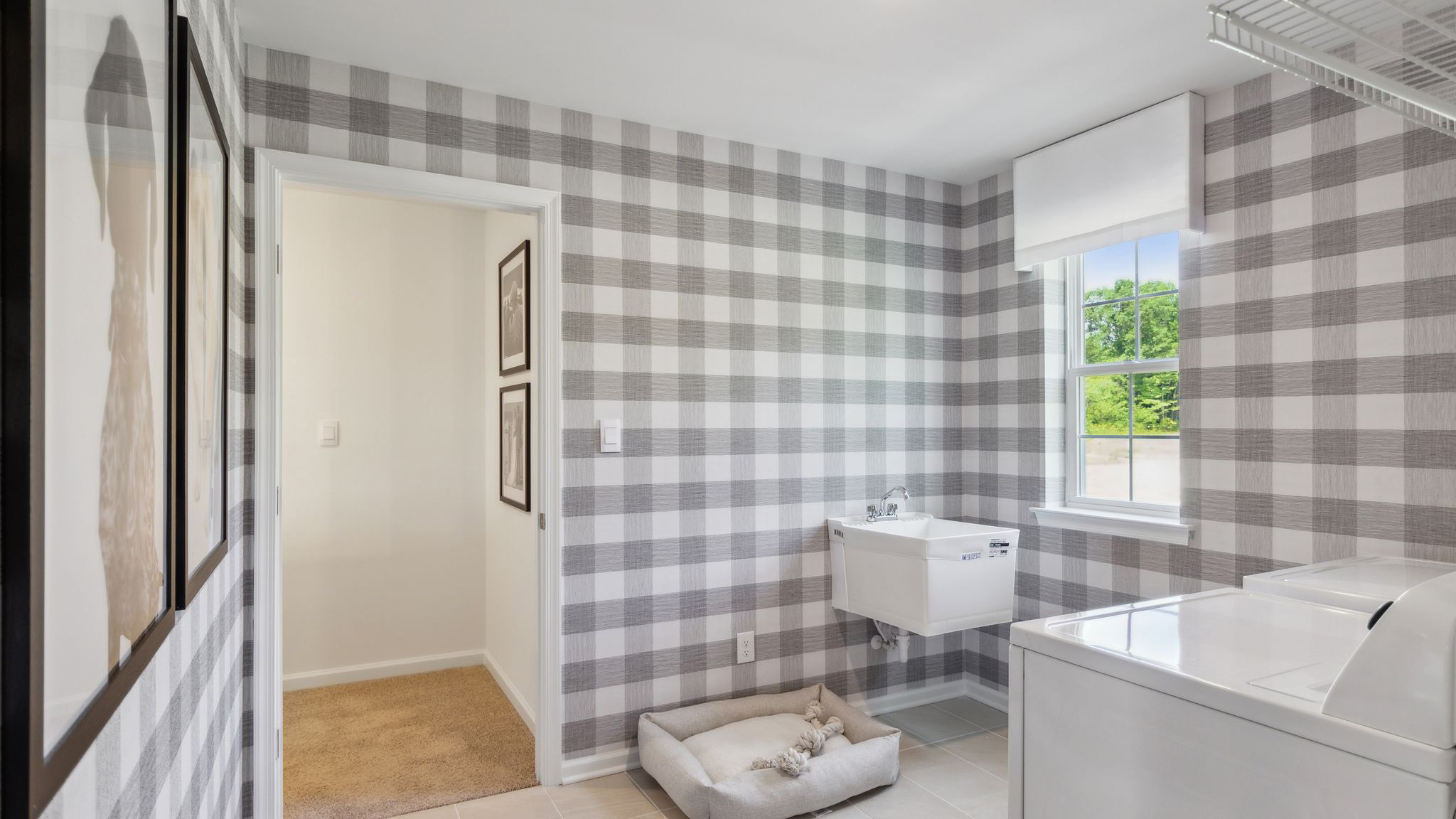 Large laundry room with full washer and dryer, stand alone sink, shelf, and single window. This room connects to the hallway next to the stairs.