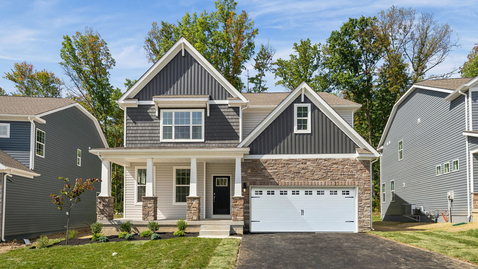 Exterior front image of a two story home in sterling horizonal siding with ironstone shake siding and board and batten accent siding and stone surrounding a white two car garage.