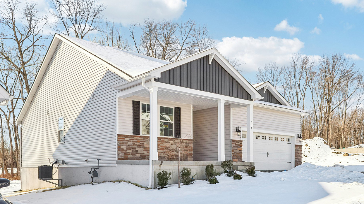 Exterior side image of the single story ranch home with sterling horizontal paneling and ironstom vertical paneling, dakota ledge stone kneewall, and a white two car garage.