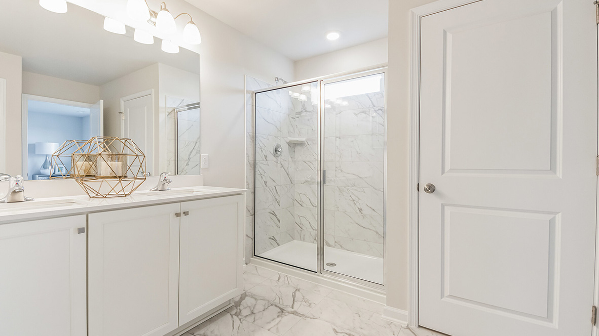 Different view of the connecting bathroom to the bedroom with two double windows. Closet in view. White and gray marble tile flooring and shower. Single white sink vanity.