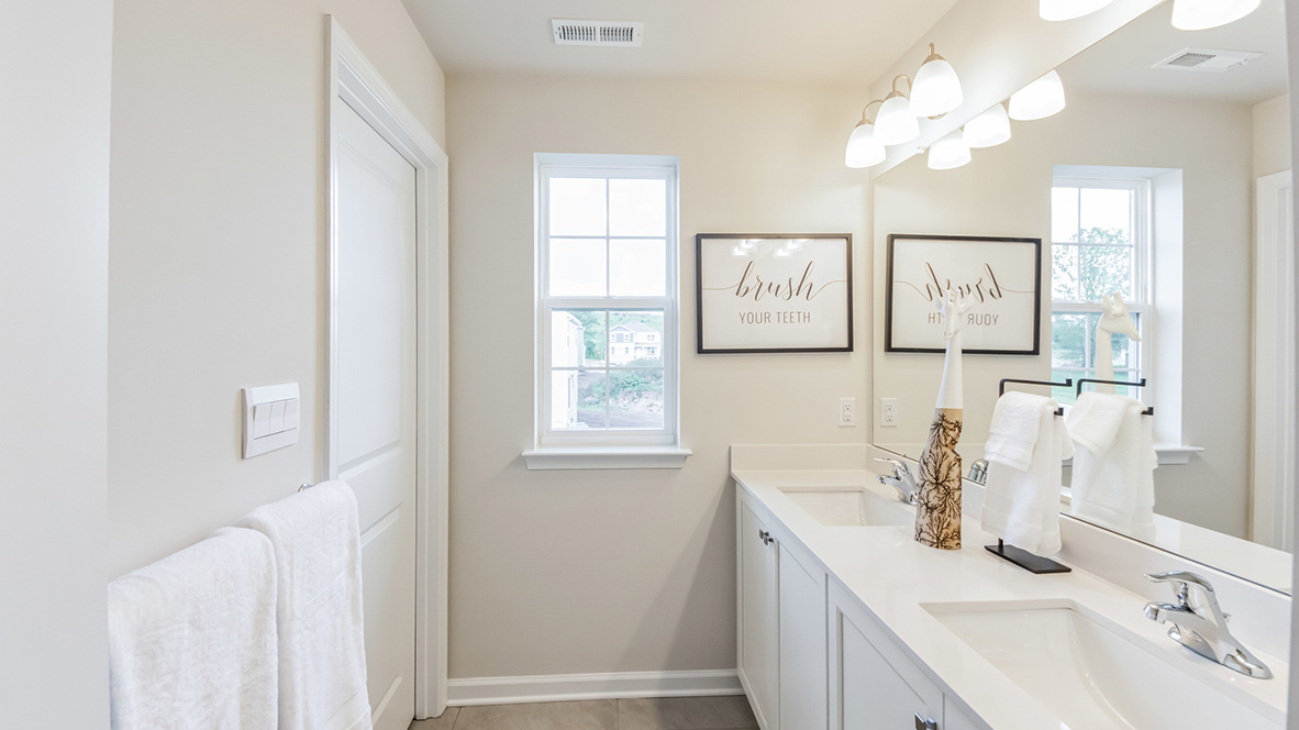 Bathroom with white double sink vanity with door separating the toilet and bathtub.