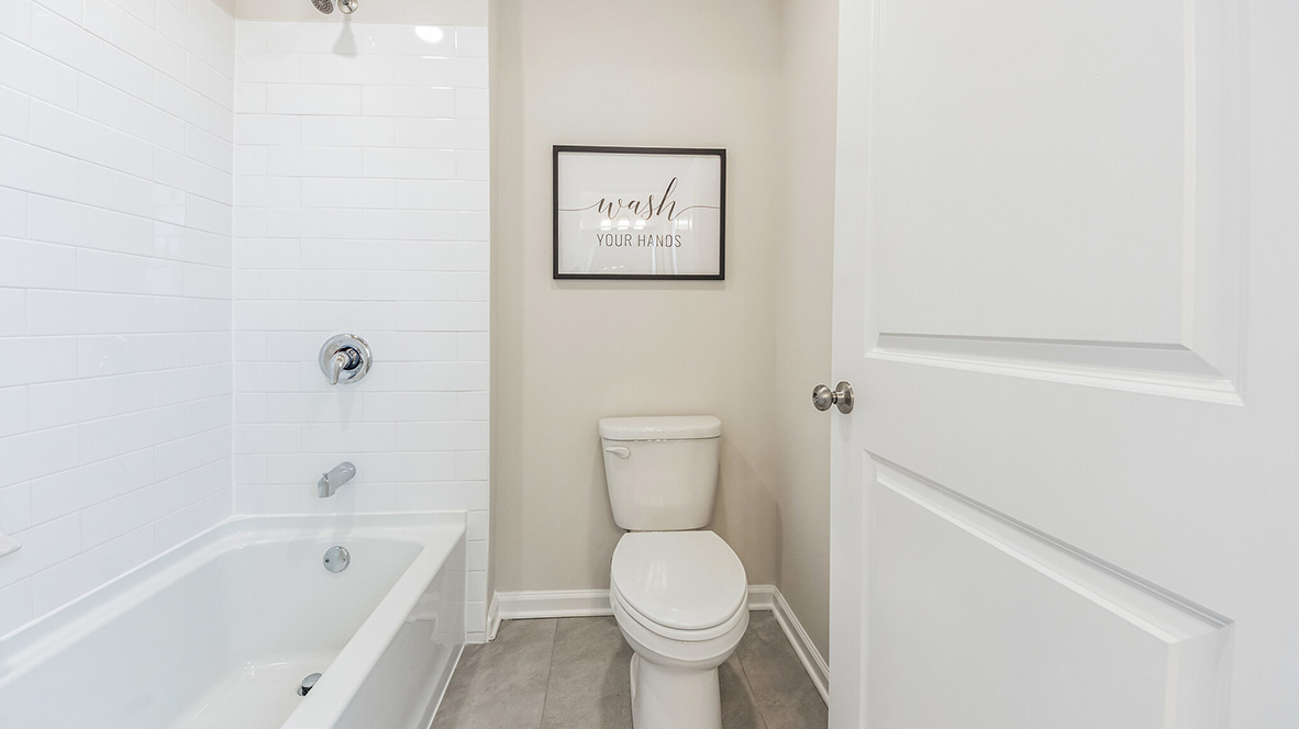 Toilet and bathtub in the room separating the bathroom with white double sink vanities.