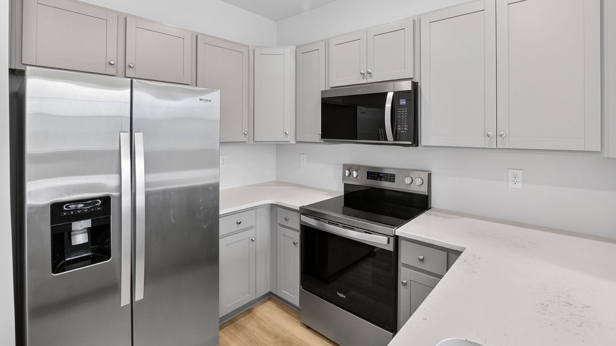 U shaped kitchen with stainless steel appliances and white counter tops and gray cabinetry.