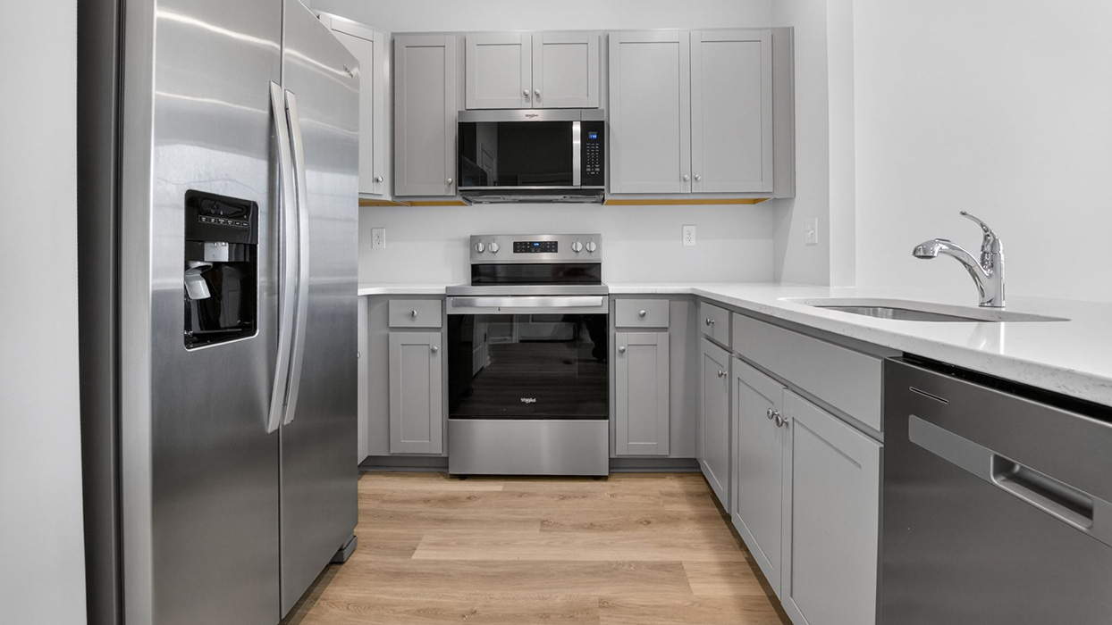 U shaped kitchen with stainless steel appliances and white counter tops and gray cabinetry.