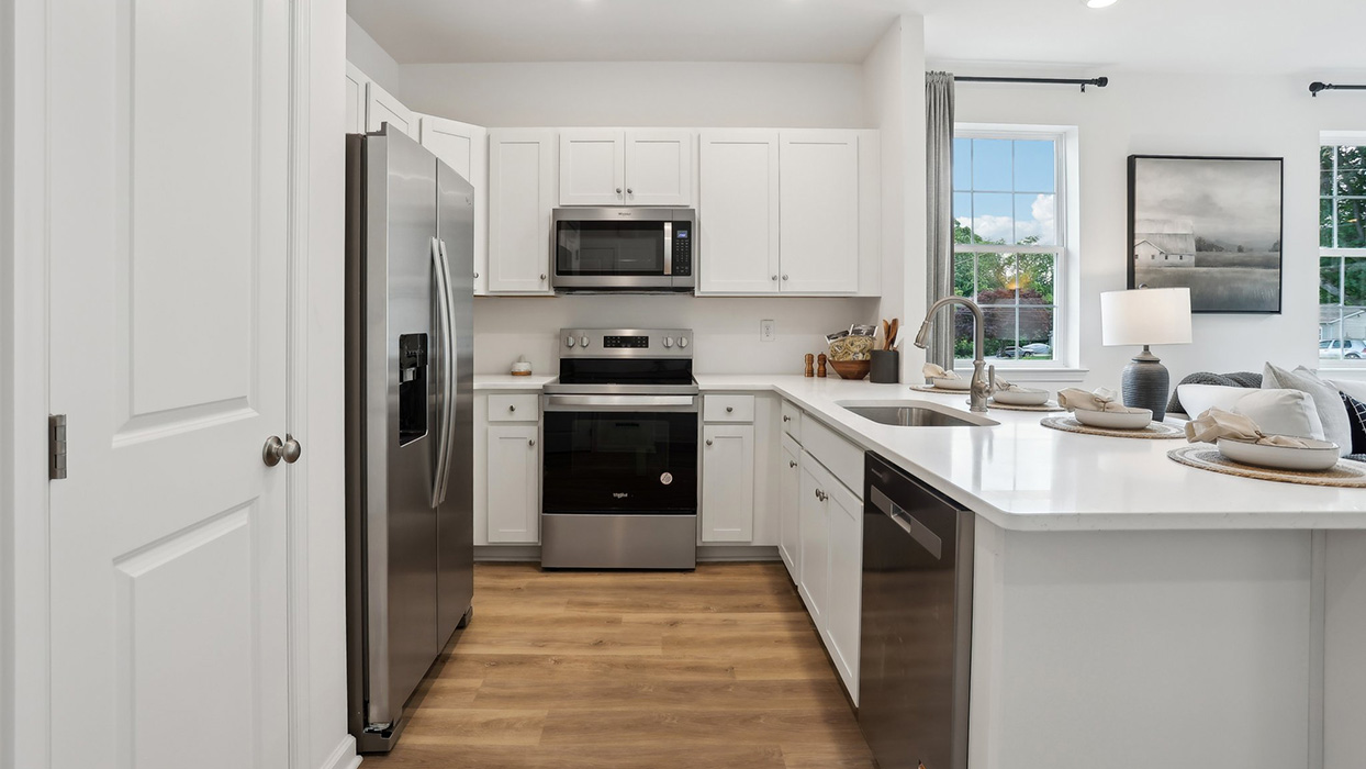 U shaped kitchen with stainless steel appliances and white counter tops and cabinetry.