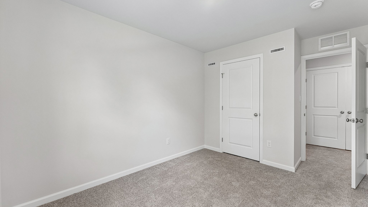 Bedroom with neutral carpeting, closet door, and hallway connection to additional rooms