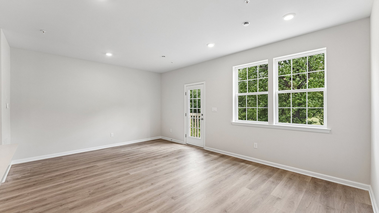 Living room with large double windows and glass door allowing natural light and views of surrounding greenery