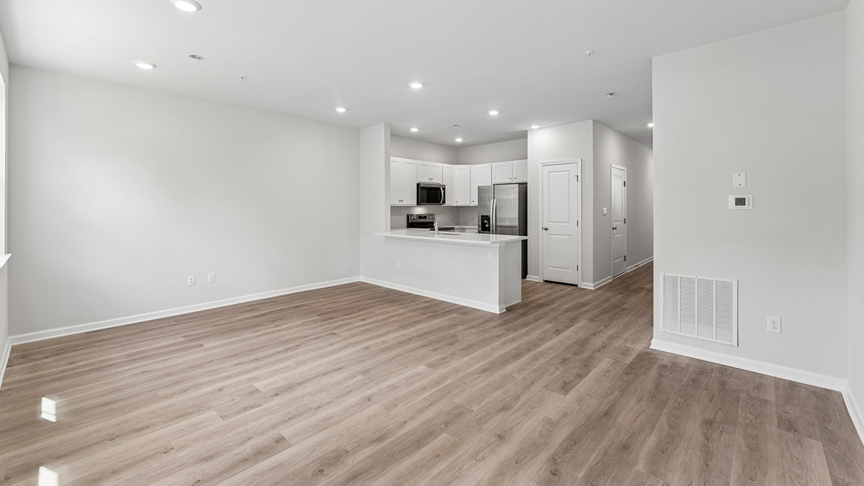 Open-concept living area with wide plank flooring, recessed lighting, and kitchen with island seating in the background