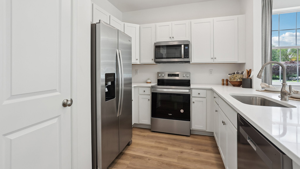 U shaped kitchen with stainless steel appliances and white counter tops and cabinetry.