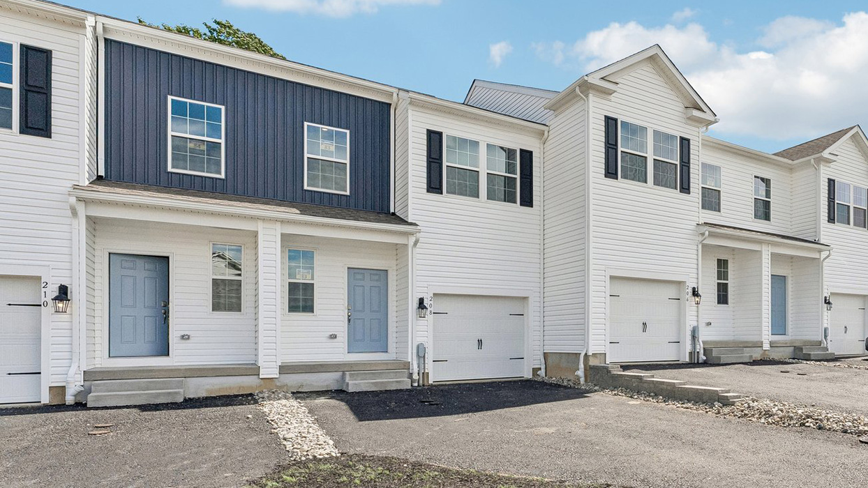Angled view of townhome row with garages, front doors, and landscaped stone borders along driveway
