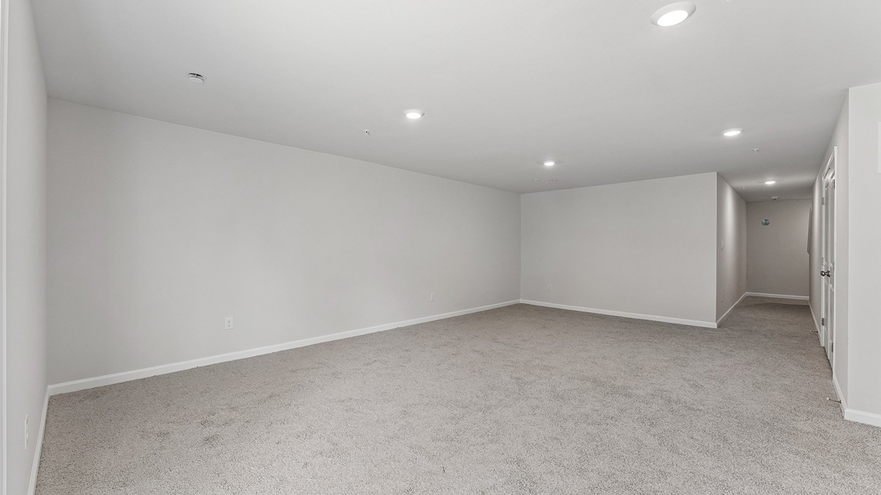 Large basement living area with open layout, recessed lighting, and hallway leading to additional rooms