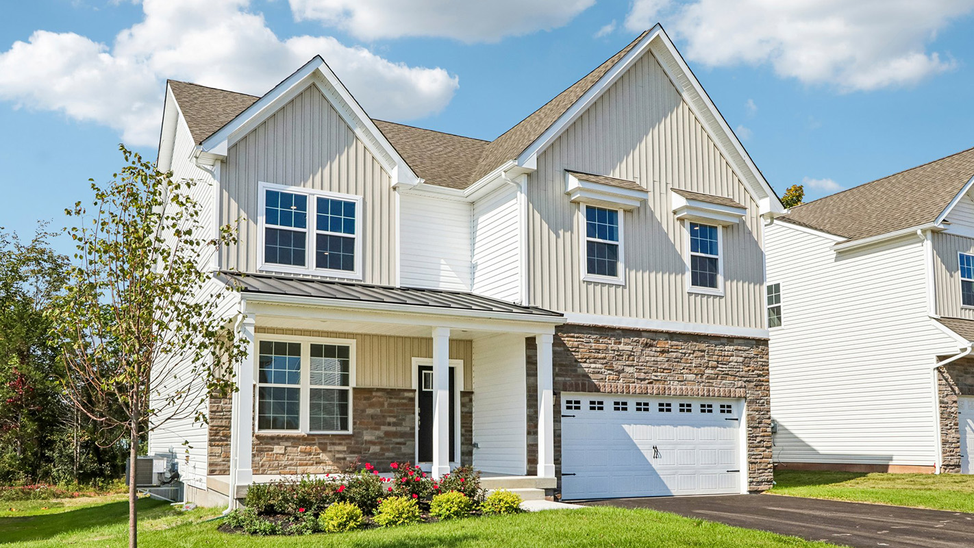Front exterior of Henley single-family home featuring cream colored siding, stone façade surrounding a two-car garage, and covered entry porch