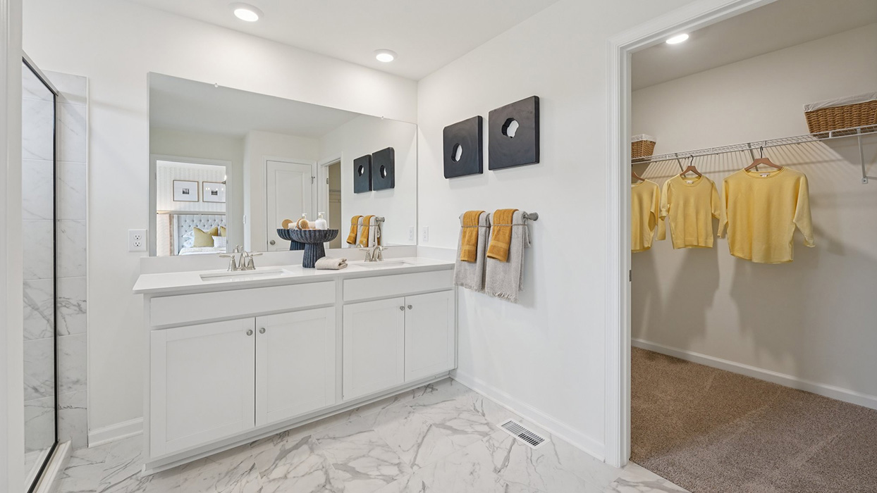 A contemporary owner’s bathroom with a peek into the owner's suite walk-in closet.