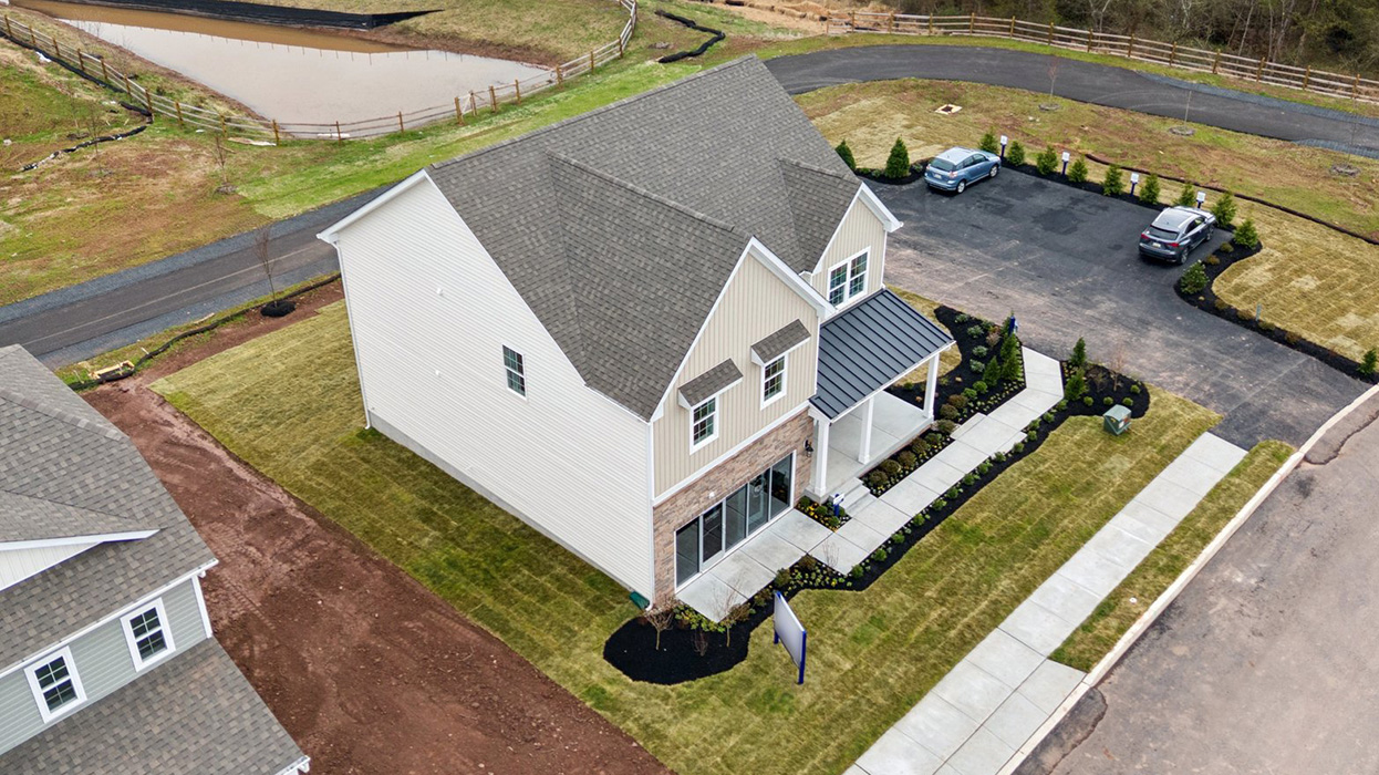 An aerial view of a two-story home with a covered front porch, horizontal plank siding in complimentary colors of linen and navy with aspen ledgestone water-table accent, and a sales center front on the two-car garage.