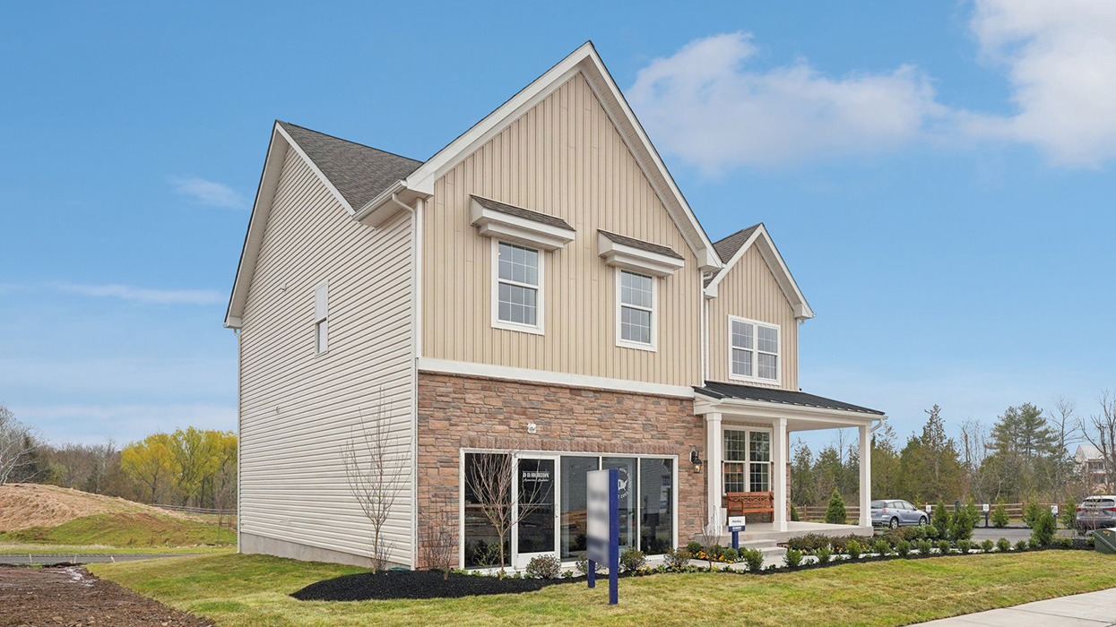 Two-story home with a covered front porch, horizontal plank siding in complimentary colors of linen and navy with aspen ledgestone water-table accent, and a sales center front on the two-car garage.