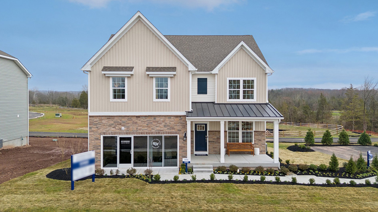 An aerial view of a two-story home with a covered front porch, horizontal plank siding in complimentary colors of linen and navy with aspen ledgestone water-table accent, and a sales center front on the two-car garage.