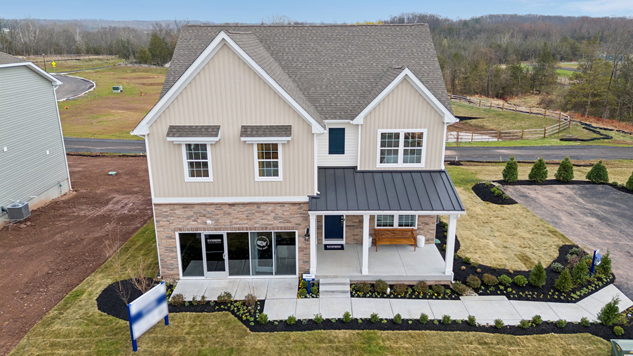 An aerial view of a two-story home with a covered front porch, horizontal plank siding in complimentary colors of linen and navy with aspen ledgestone water-table accent, and a sales center front on the two-car garage.