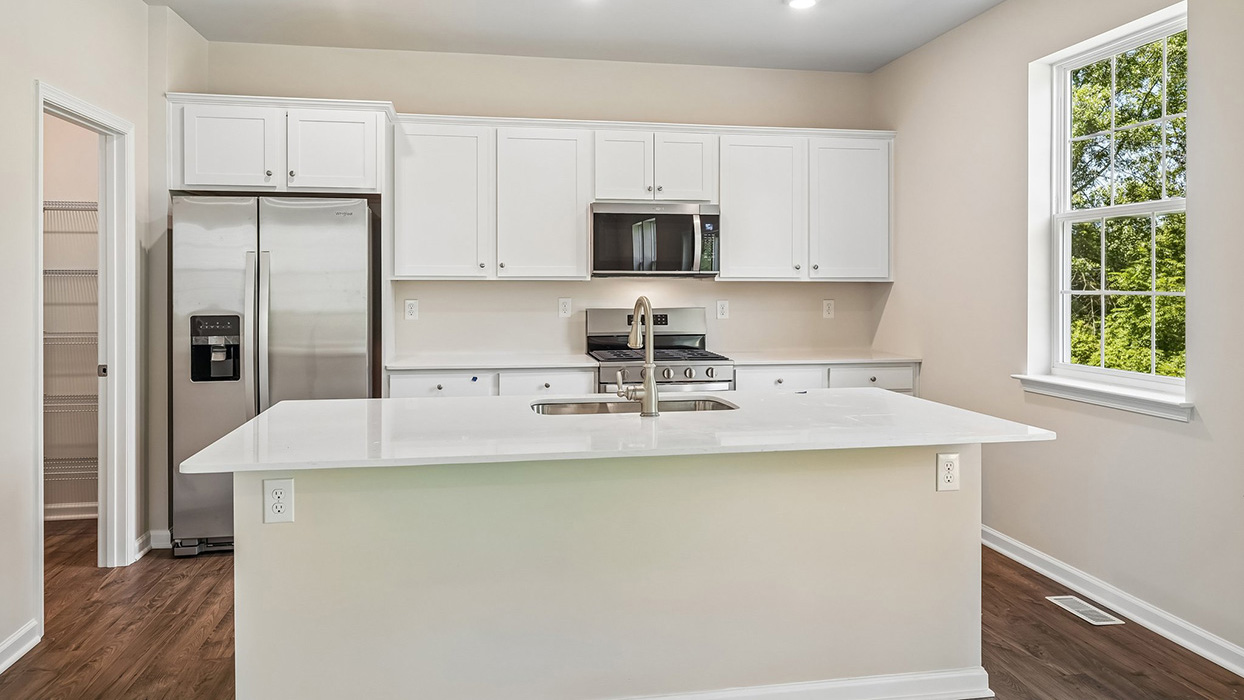 Open kitchen and dining area in the Galen single-family home at Creekside Village featuring a large center island, stainless steel appliances, and sliding glass door with backyard views.