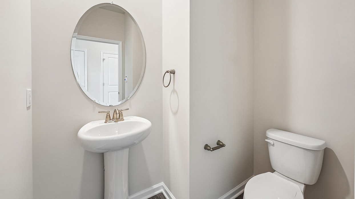 Powder room in the Galen single-family home at Creekside Village featuring a pedestal sink, oval mirror, brushed nickel fixtures, and neutral finishes.