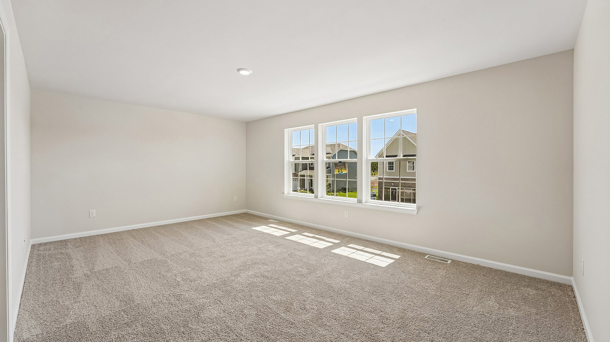 Spacious owner's suite in the Galen single-family home at Creekside Village with plush carpeting, abundant natural light, and three large windows.