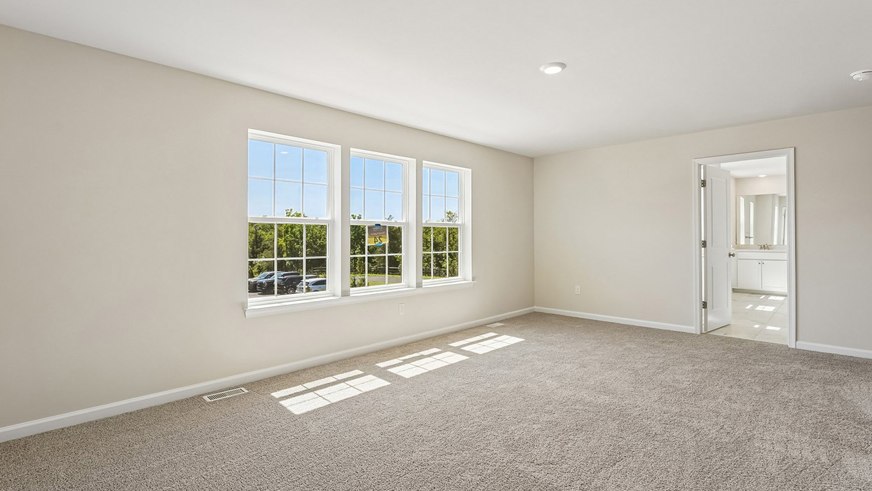 Owner's bedroom in the Galen single-family home at Creekside Village featuring large windows, plush carpeting, and direct access to the en suite bathroom.
