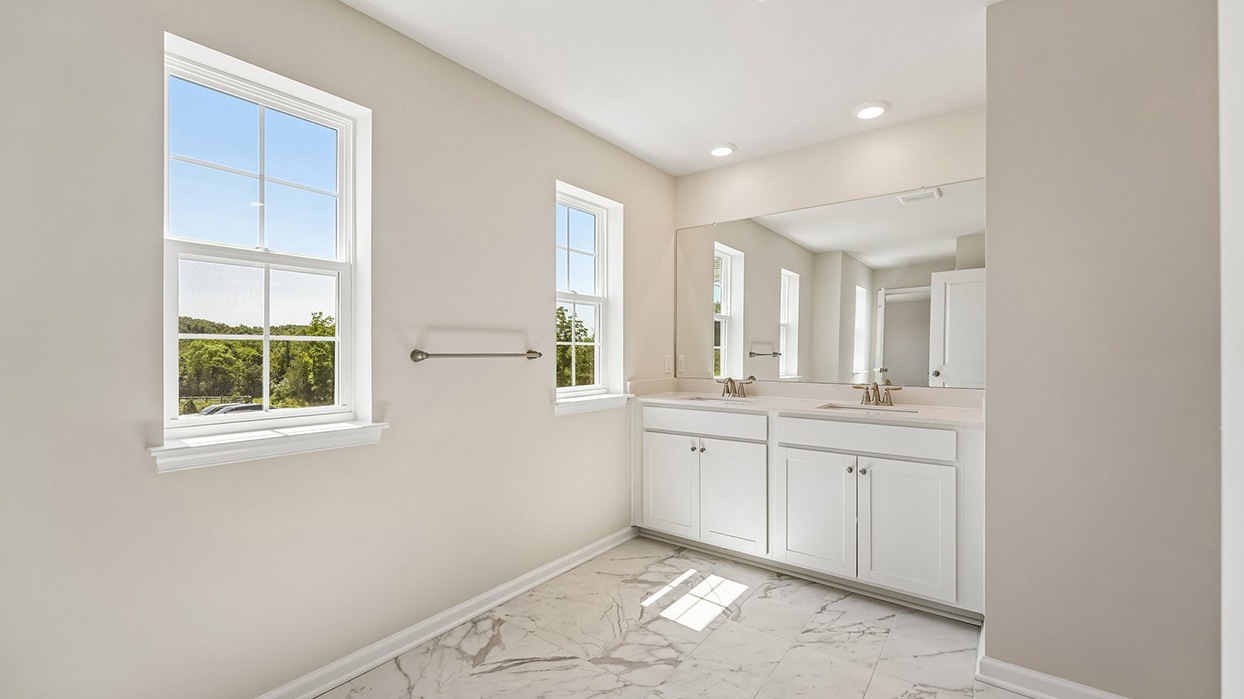 Owner's bathroom in the Galen single-family home at Creekside Village featuring dual vanities, marble-look tile flooring, and large windows for natural light.