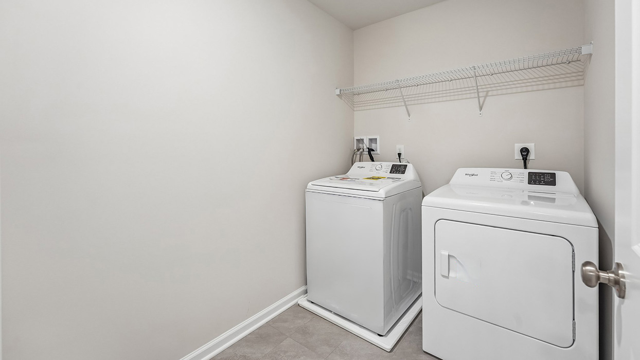 Convenient second-floor laundry room in the Galen single-family home at Creekside Village featuring a washer, dryer, and wire shelving for storage.