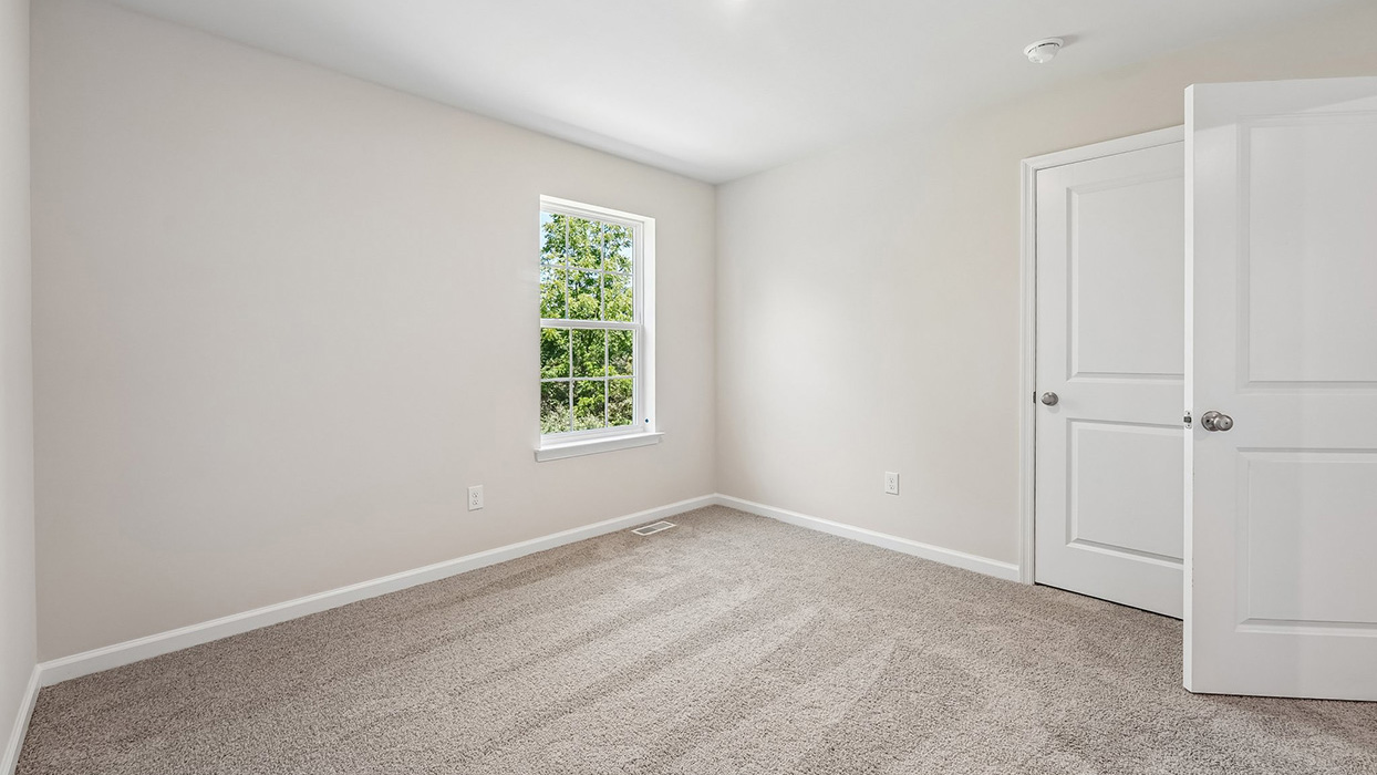 Bright secondary bedroom in the Galen single-family home at Creekside Village featuring neutral finishes, plush carpeting, and natural light.